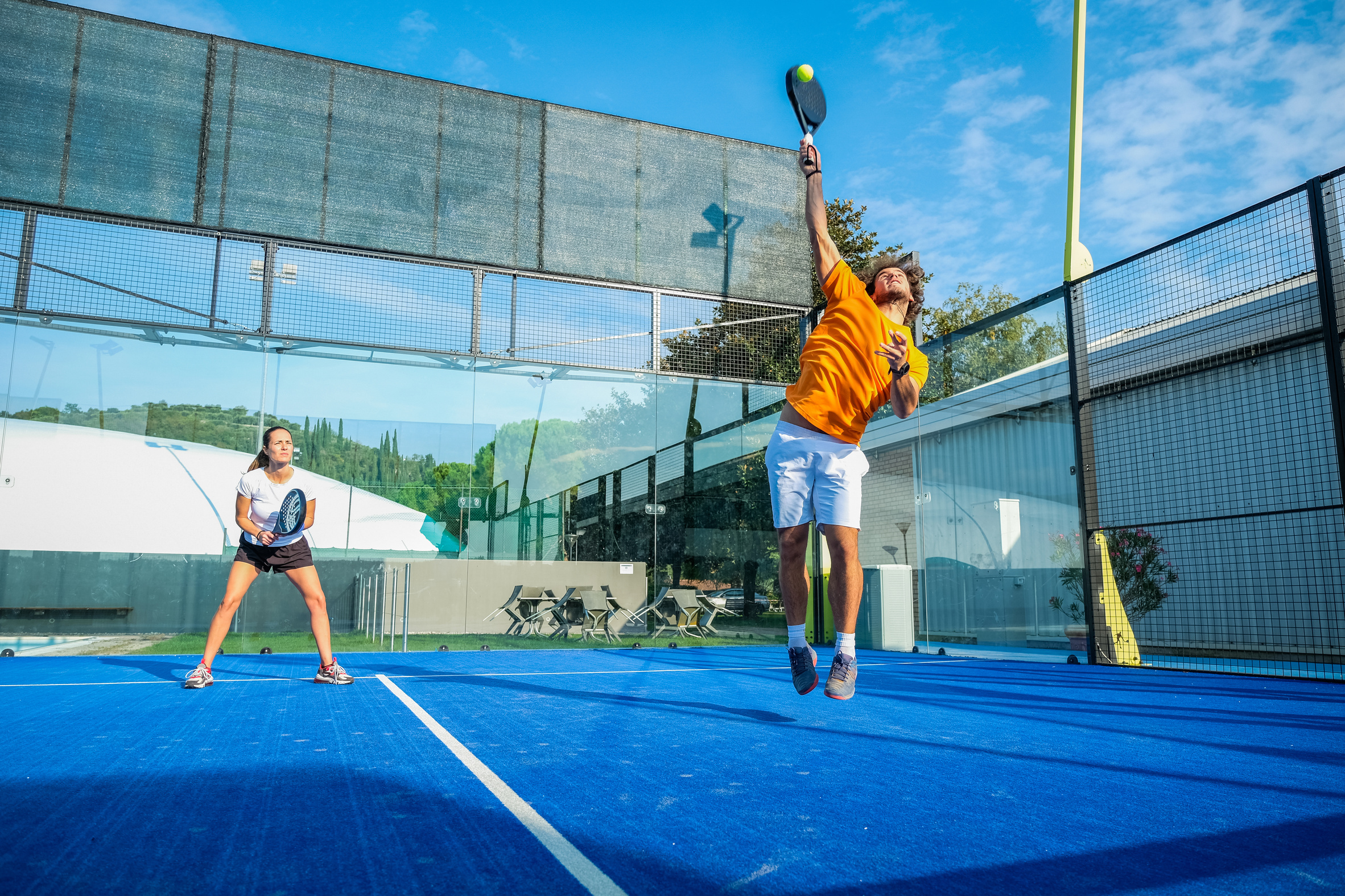 Mixed padel match in a blue grass padel court - Beautiful girl and handsome man playing padel outdoor